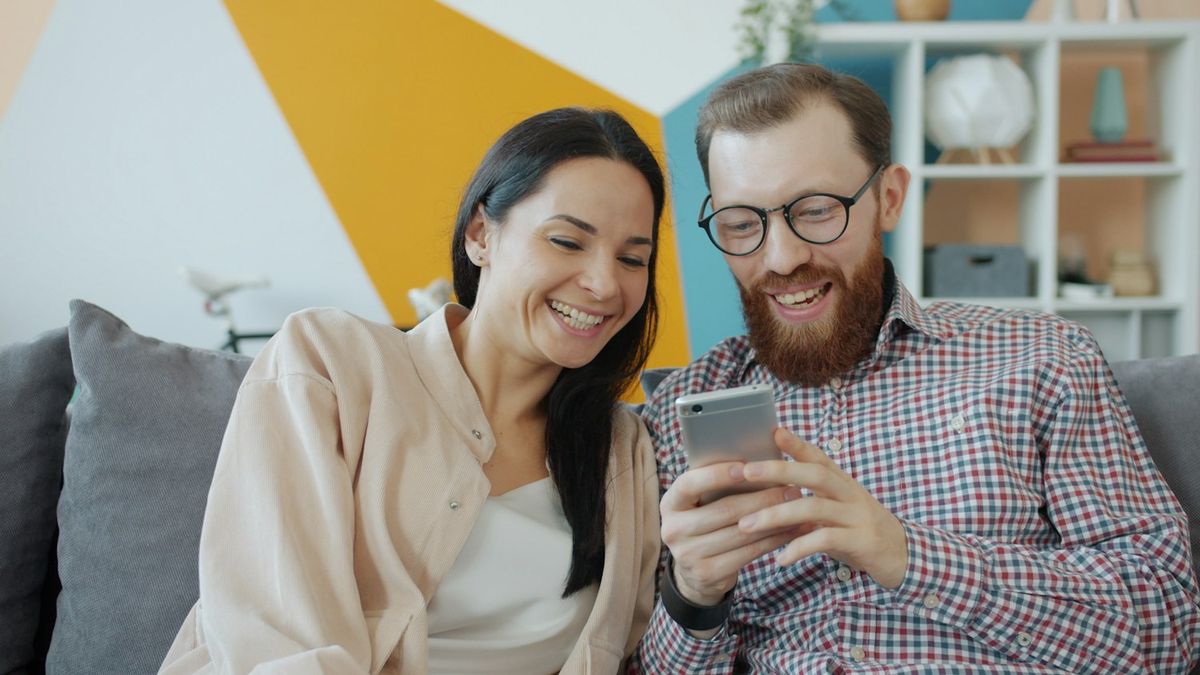 Pareja riéndose mientras mira el celular en el sofá